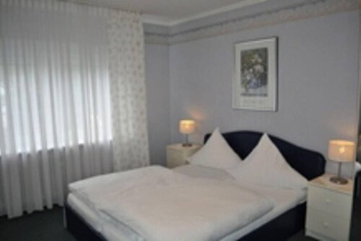A hotel room with a neatly made bed, two bedside tables with lamps, a framed picture on the wall, and a window with curtains.