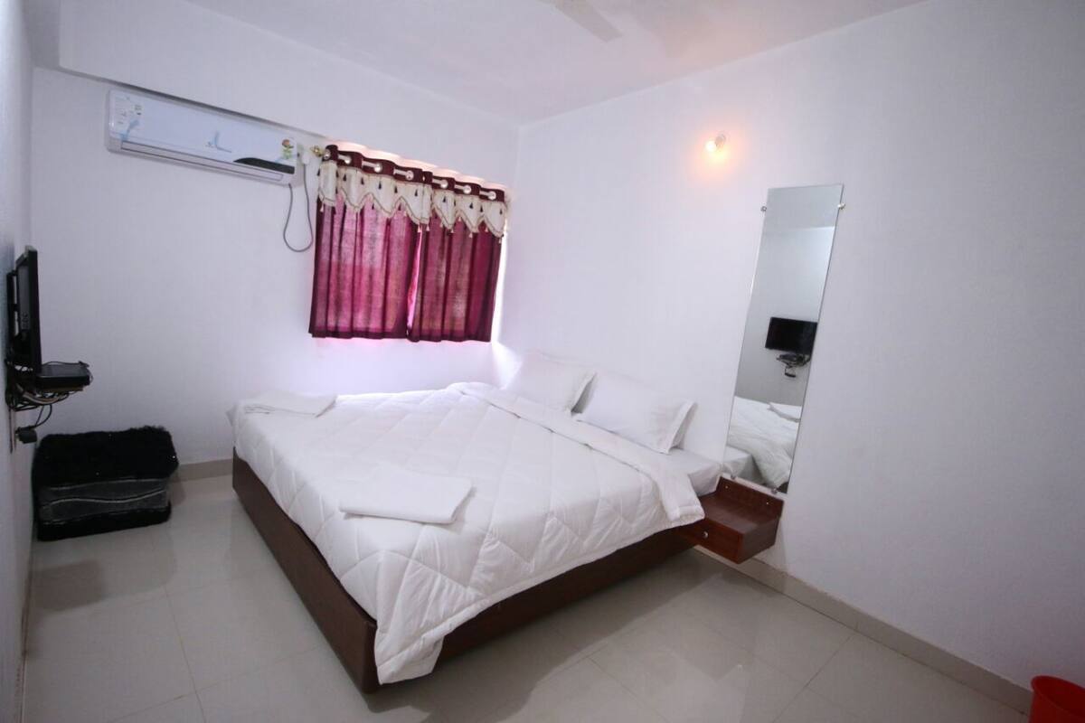 A hotel room with a large bed, a bedside table, a mirror, a wall-mounted air conditioner, and a curtain.
