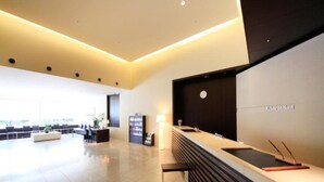 Zona de recepción de un hotel moderno con un diseño limpio y minimalista, que incluye mostrador de recepción, área de estar y un reloj en la pared.