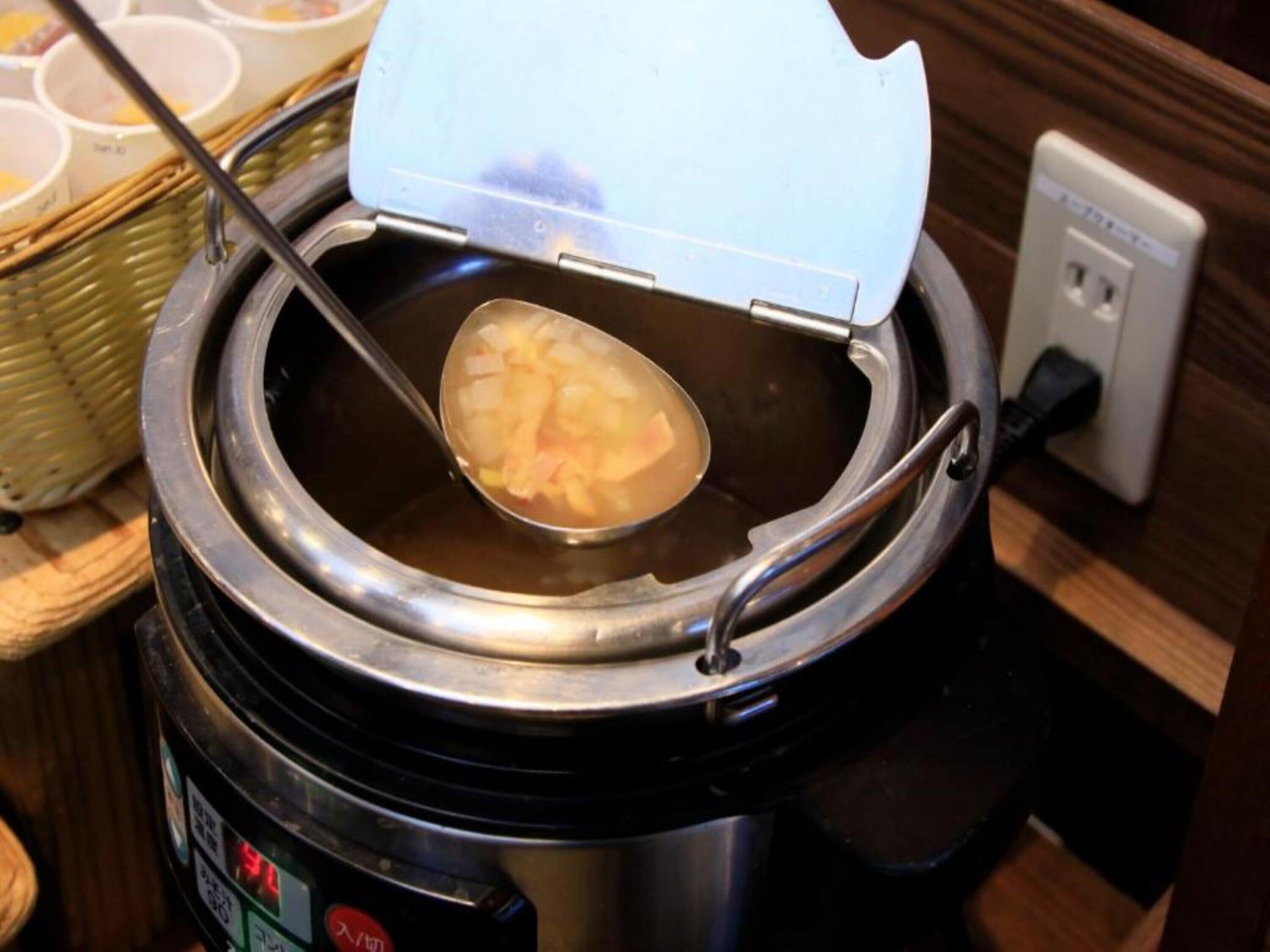 A portable electric rice cooker with a lid open, revealing cooked rice inside.