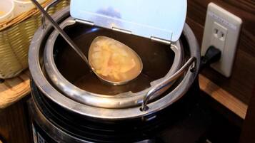 A portable electric rice cooker with a lid open, revealing cooked rice inside.