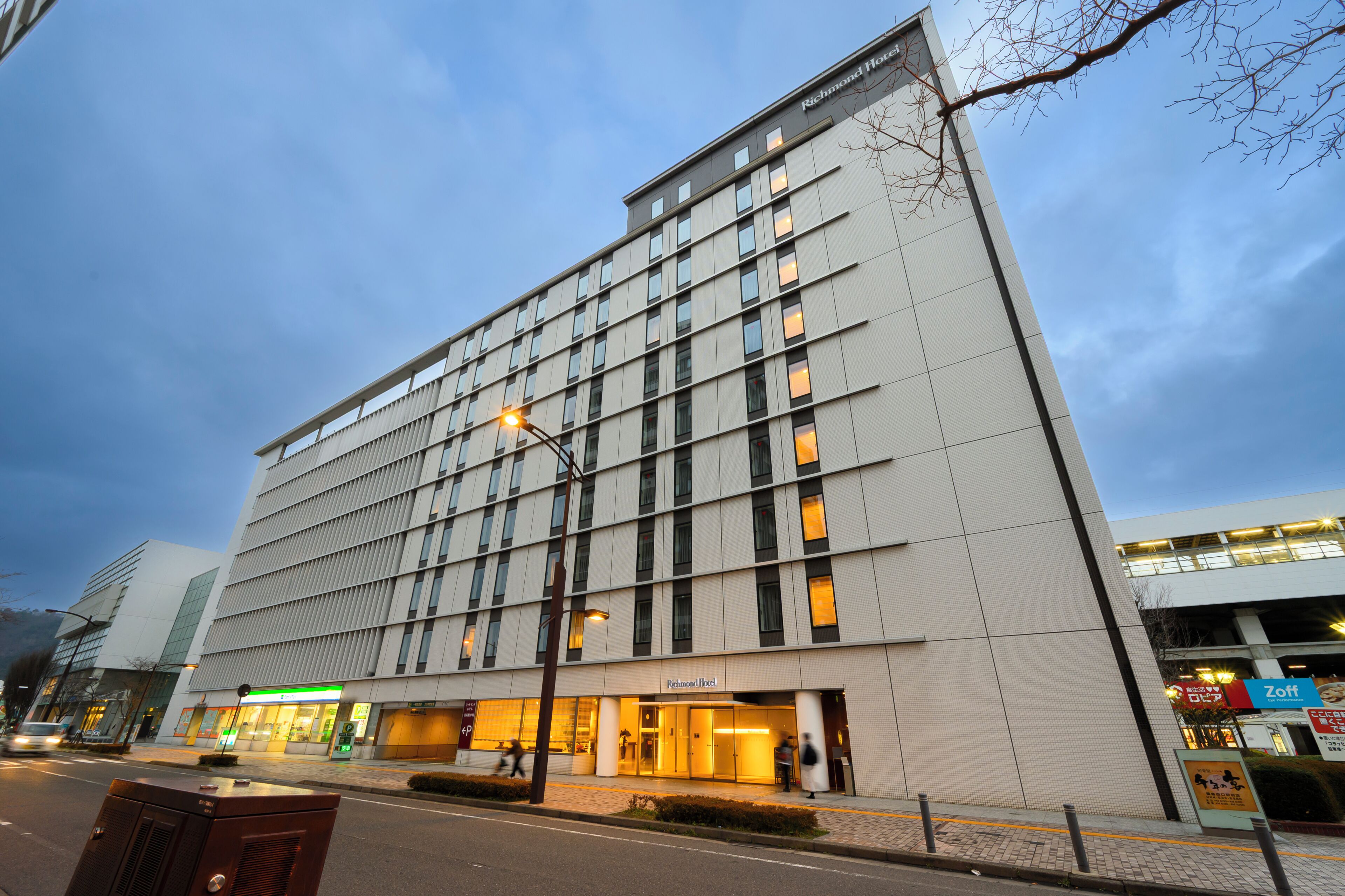 A modern hotel building with a prominent entrance, a visible restaurant named 'Zoft' across the street, and a clear sky.