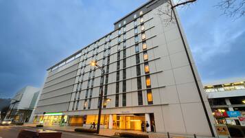 A modern hotel building with a prominent entrance, a visible restaurant named 'Zoft' across the street, and a clear sky.