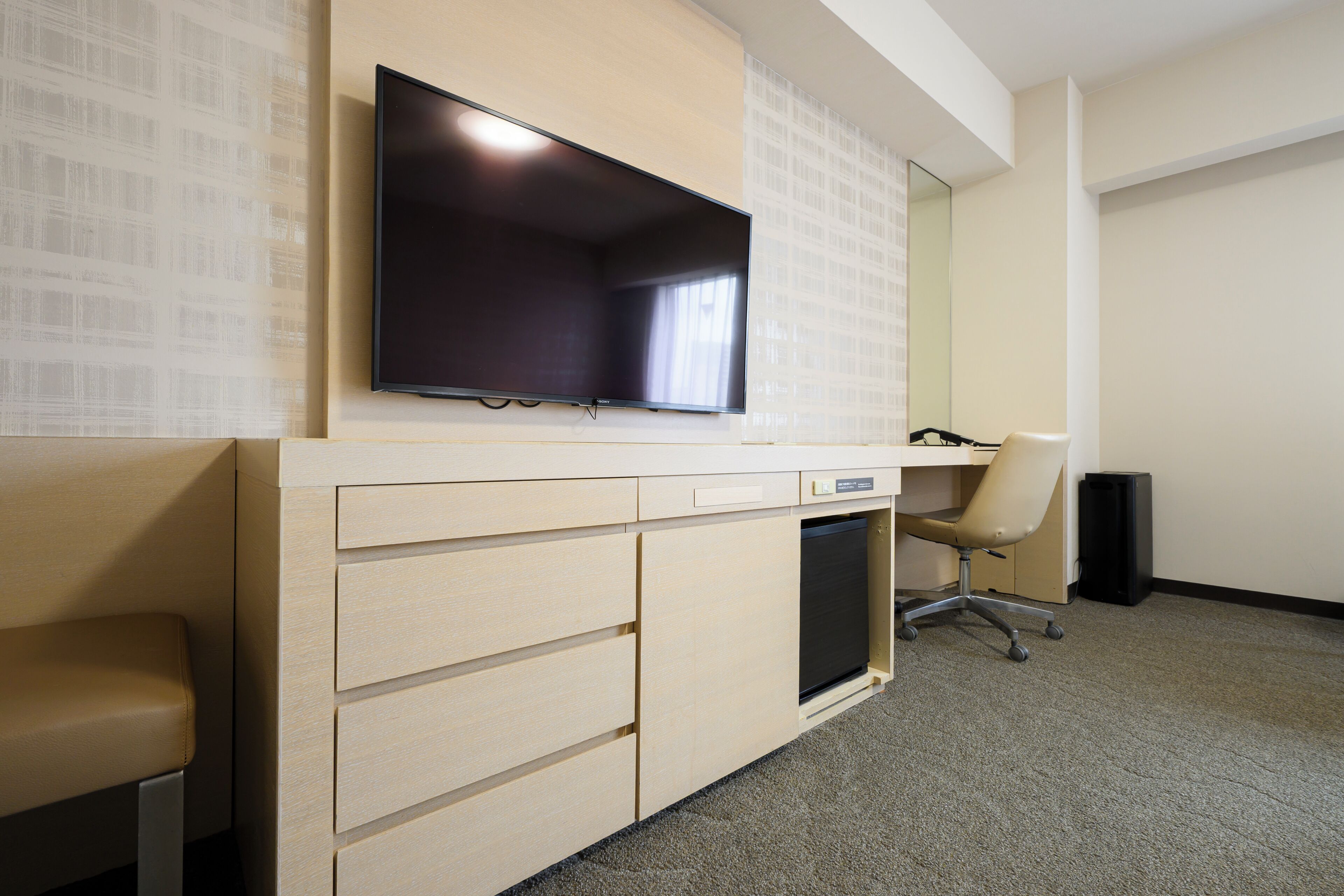 Habitación de hotel con televisor de pantalla plana montado en la pared, un escritorio con silla y un mueble auxiliar pequeño.