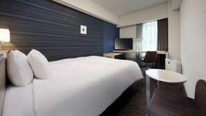 Habitación de hotel con una cama grande, un escritorio, una silla, una mesita, un televisor y una ventana con cortinas.