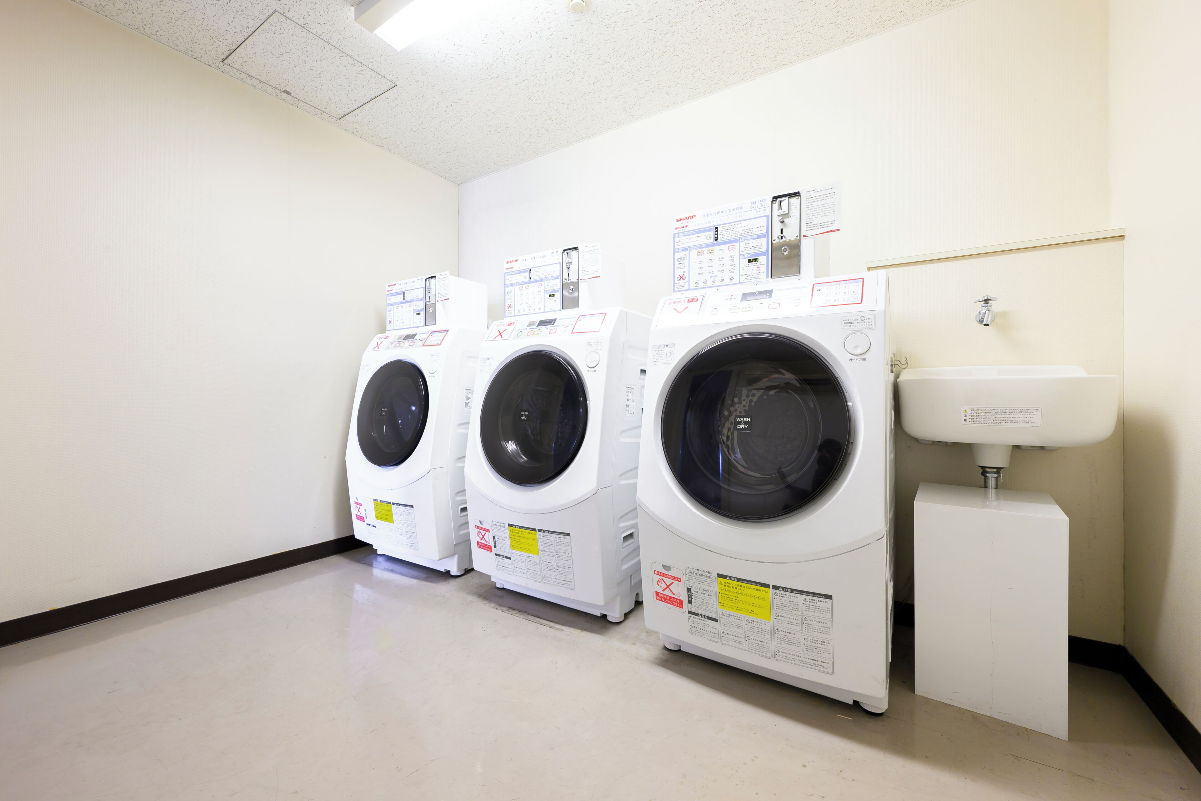 A laundry room with three stacked washing machines and a sink.