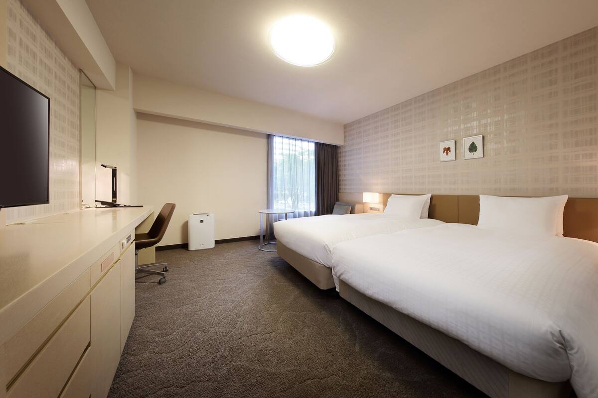 Habitación de hotel con una cama grande, un escritorio con una silla, una mesita y un televisor.