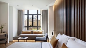 A modern hotel room with a large bed, a sofa, a small table, and a view of the city through large windows. - The Editor Hotel Athens (Athens)