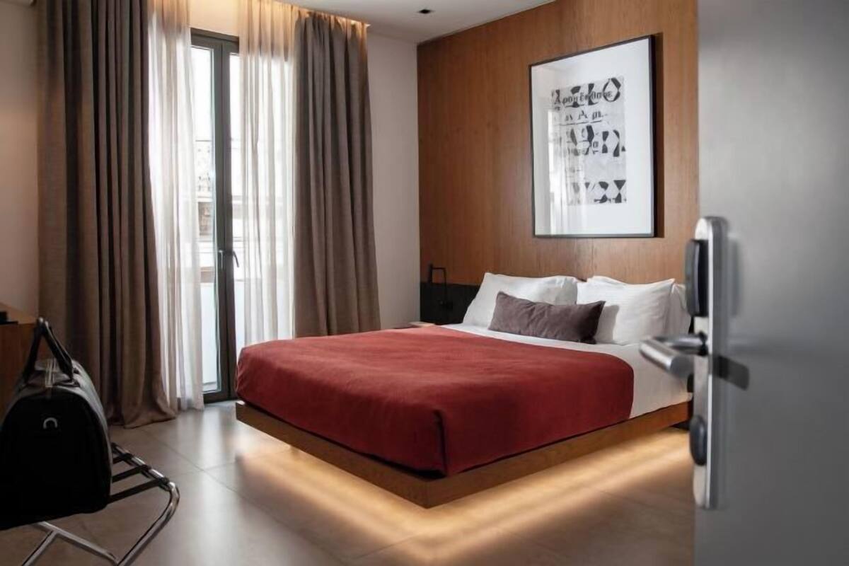 Una habitación de hotel moderna con cama, cortinas, un cuadro enmarcado y un carrito de equipaje.
