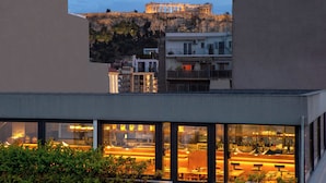 A modern building with large windows overlooking a restaurant with outdoor seating. - The Editor Hotel Athens (Athens)