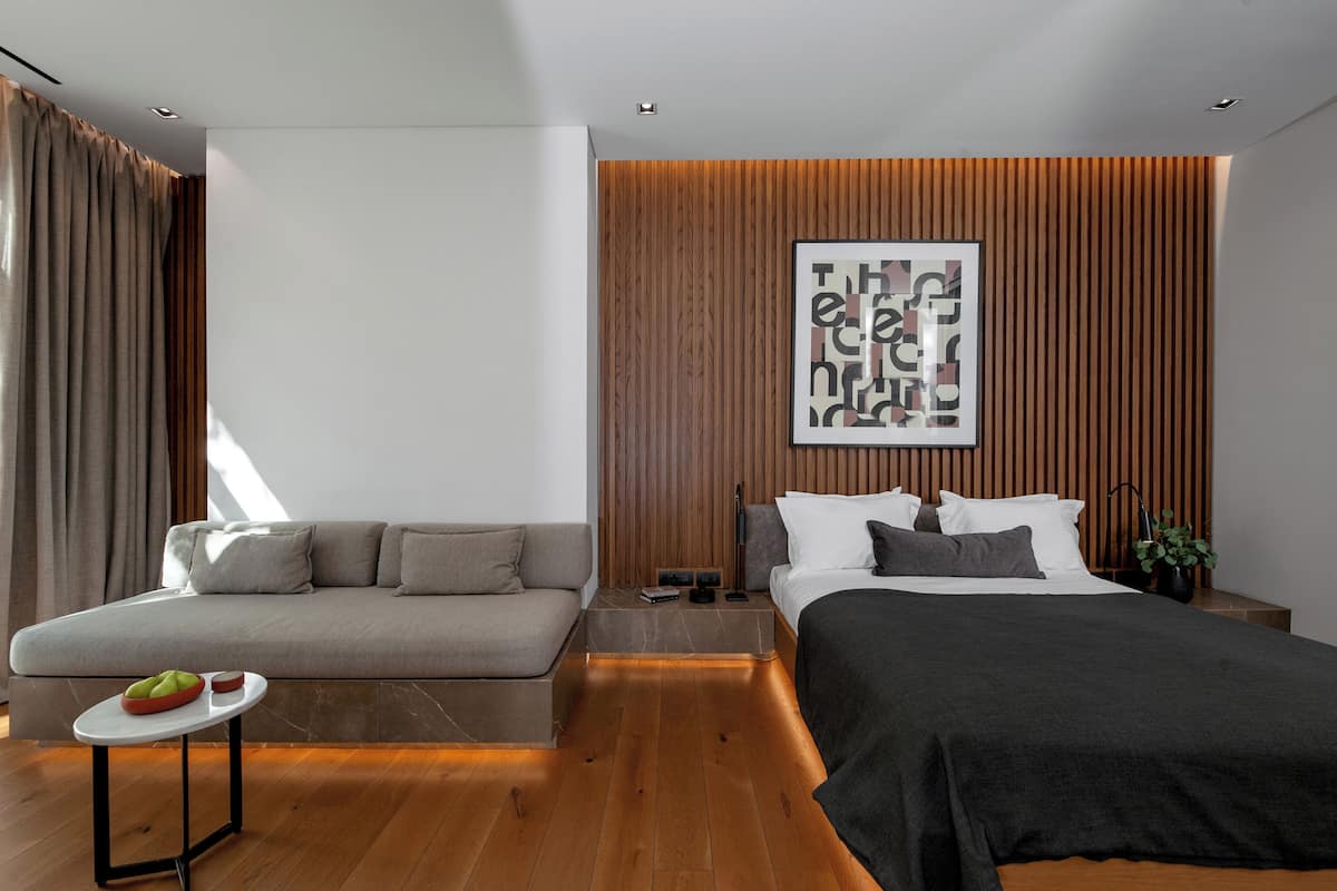 Un dormitorio moderno con un sofá, una cama, una mesita con un frutero y una obra de arte colgada en la pared.