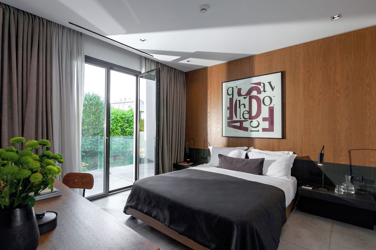 Habitación de hotel moderna con una cama grande, un revestimiento de pared de madera y vistas a la vegetación a través de una puerta corredera de vidrio.