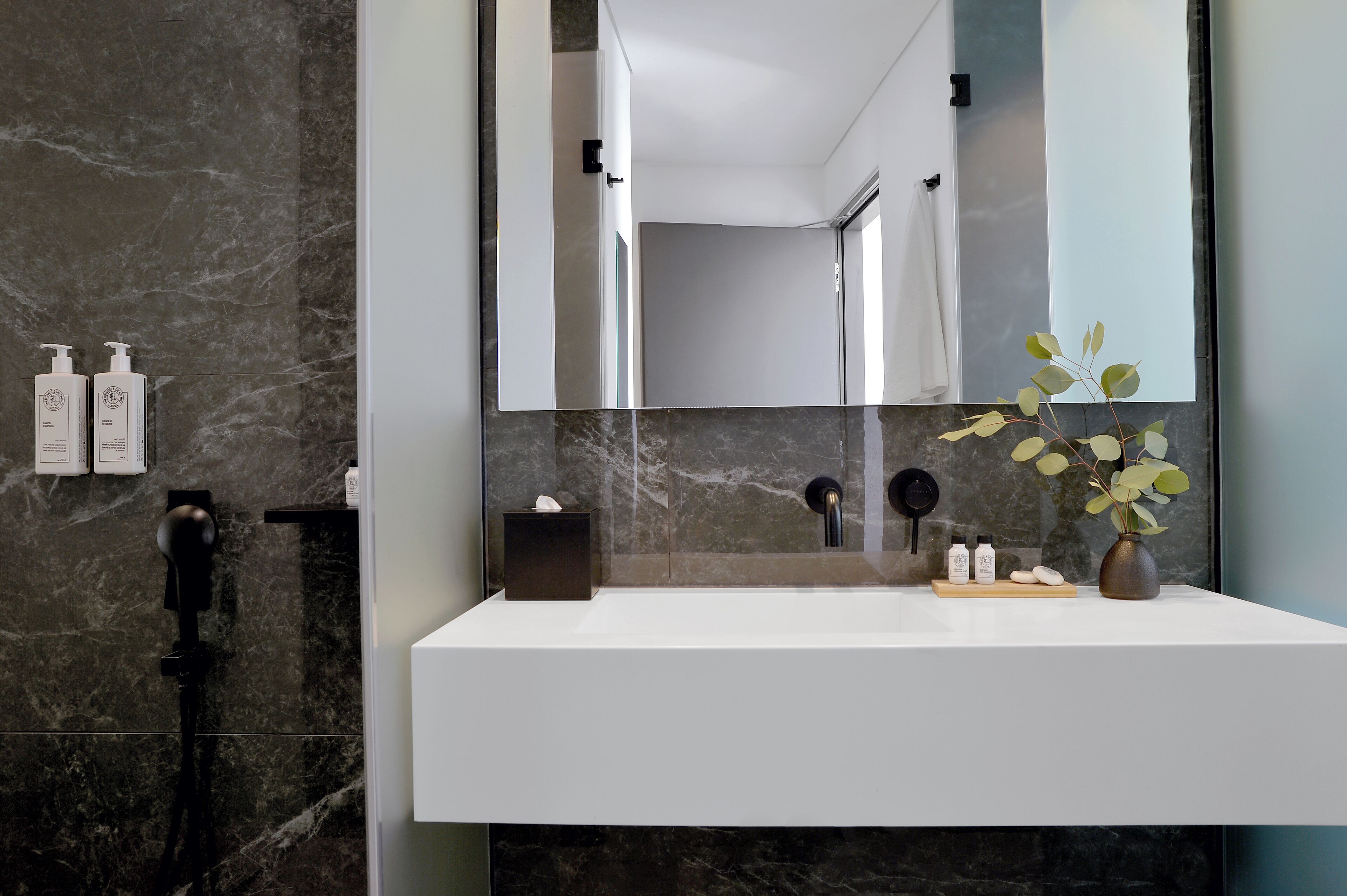 Un baño moderno con pared de mármol, un espejo grande, un lavamanos blanco y un perchero para toallas.