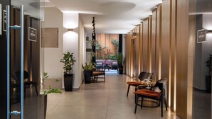 A modern hotel lobby with a glass wall, wooden paneling, and a seating area with a table and chairs. - The Editor Hotel Athens (Athens)