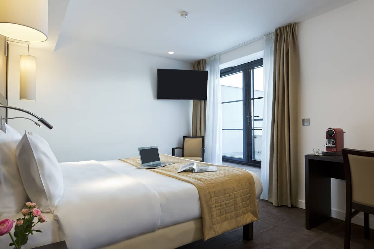 A hotel room with a bed, a desk, a laptop, a coffee maker, and a TV.