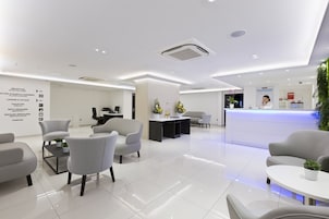A modern hotel lobby with a reception desk, seating area, and directional signage.
