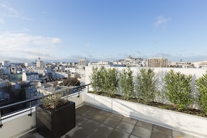 A rooftop terrace with a city view, potted plants, and a railing.