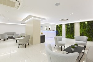 A modern reception area with a white reception desk, several seating options, and a green wall with a vertical garden.