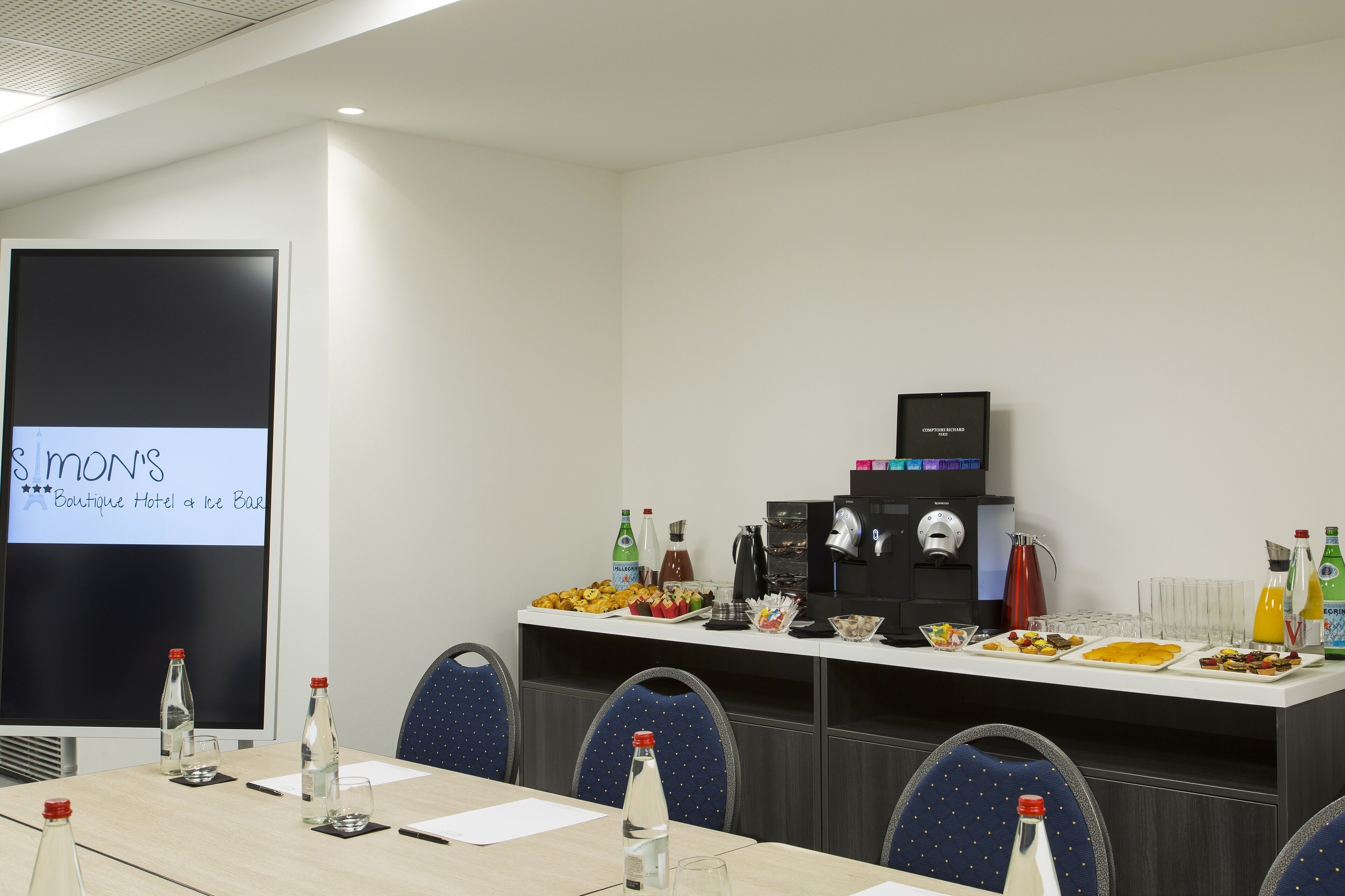 Een vergaderruimte met een presentatiescherm, een buffet met diverse gerechten en een koffiehoek.