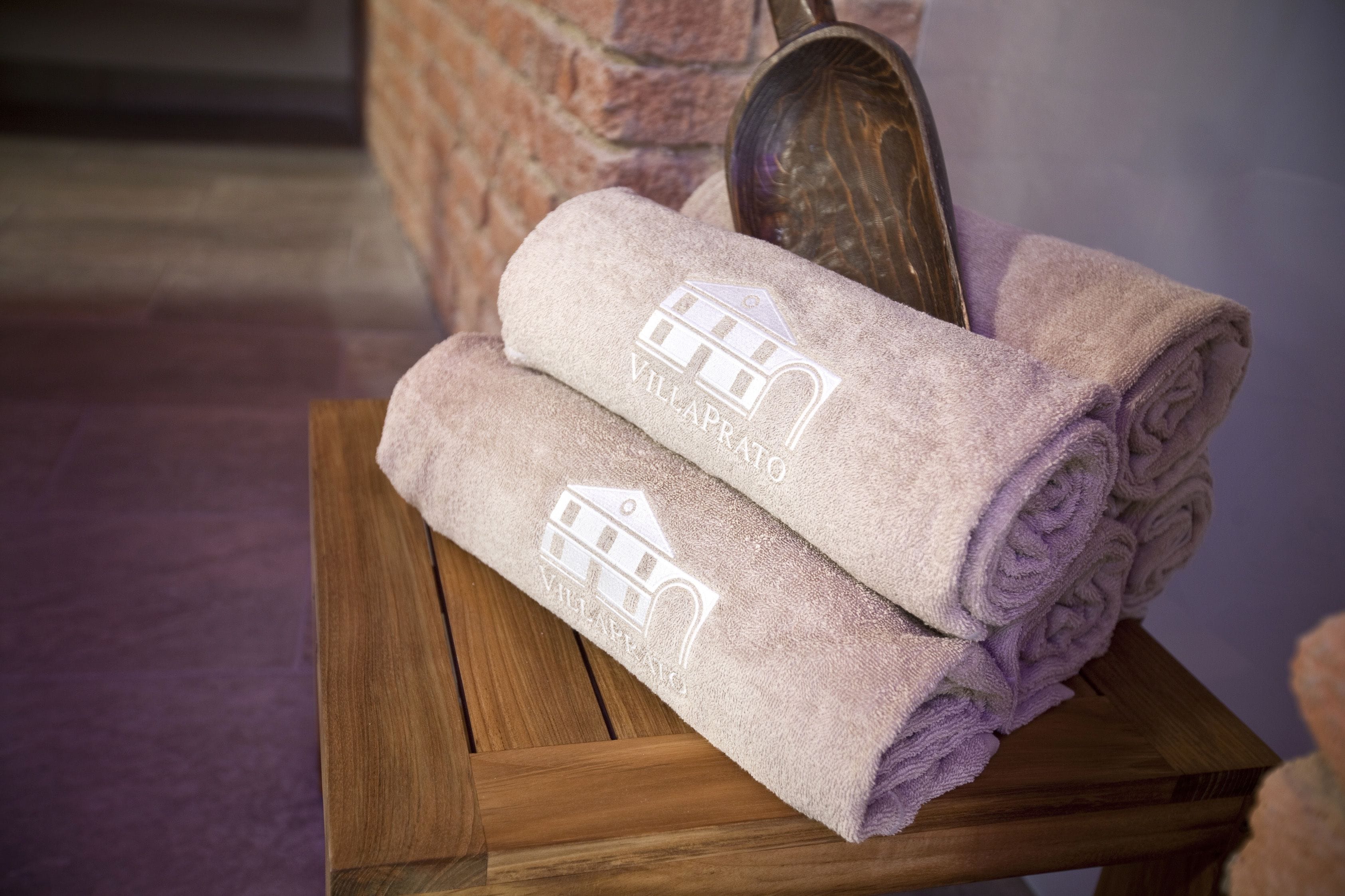 Two rolled towels with a building logo on a wooden stool.