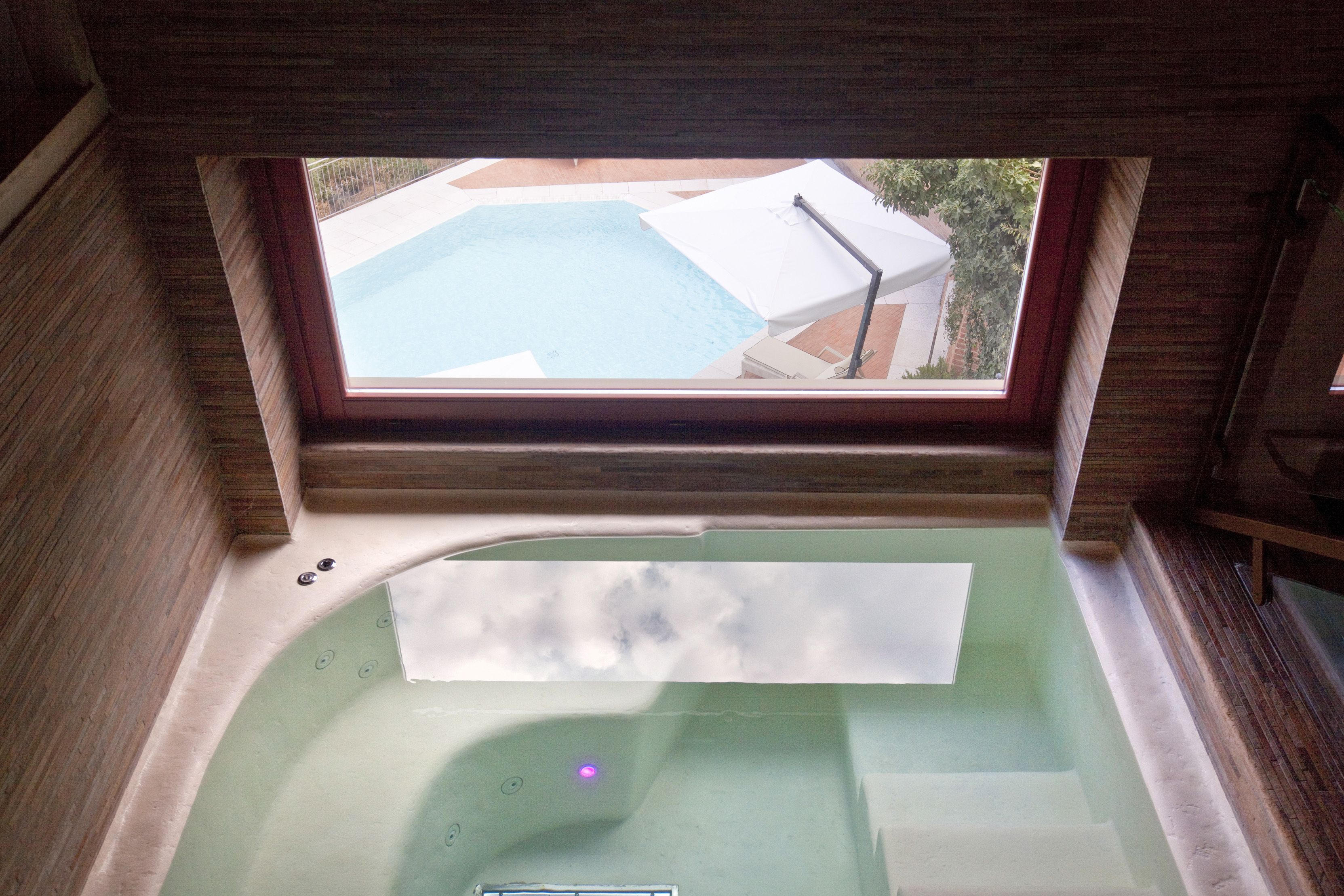 En vy genom ett fönster som visar en del av ett spa med ett bubbelbad och en pool.