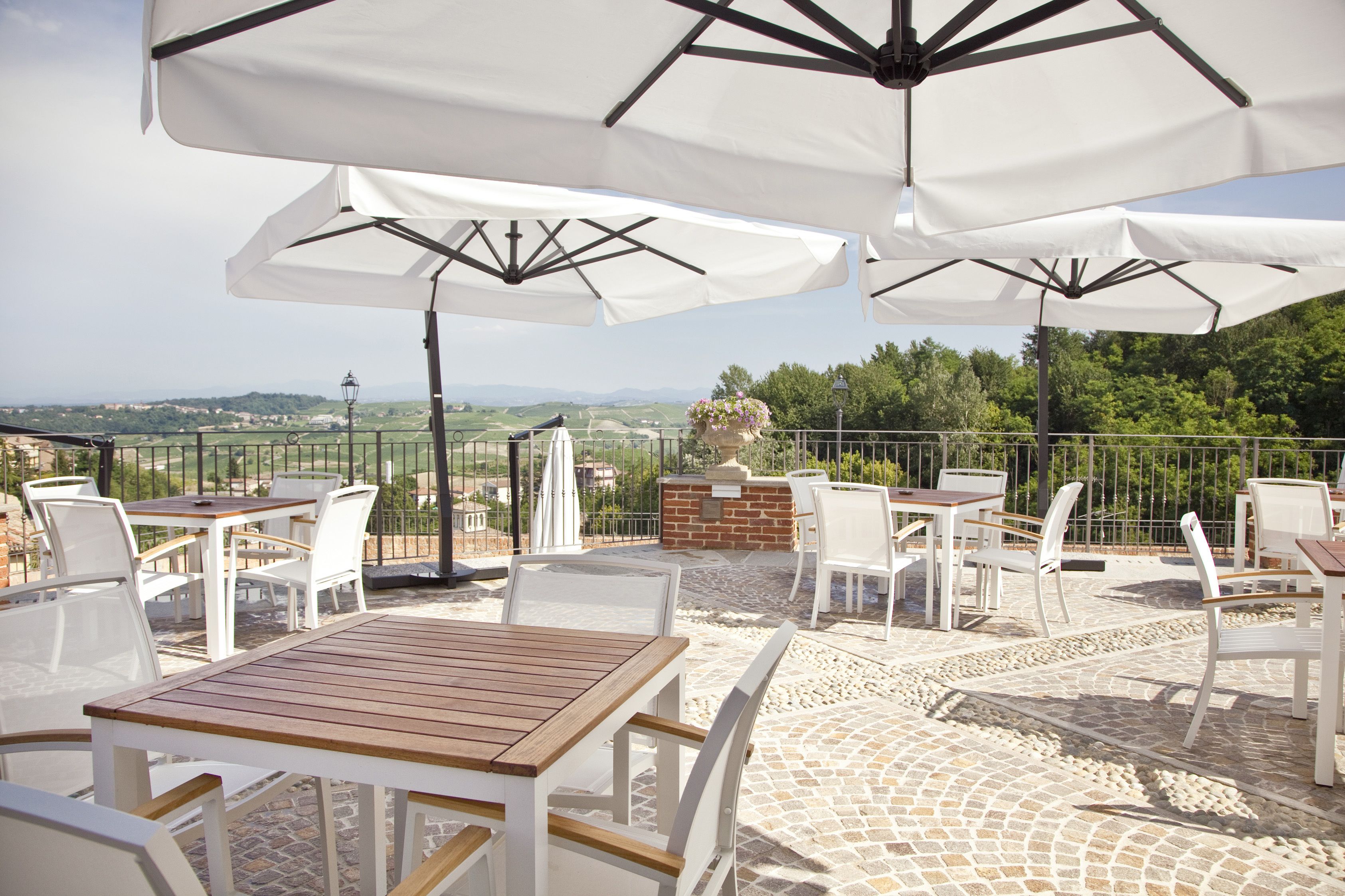 An outdoor patio with white tables and chairs, white umbrellas, and a view of the countryside.