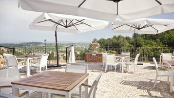 An outdoor patio with white tables and chairs, white umbrellas, and a view of the countryside.