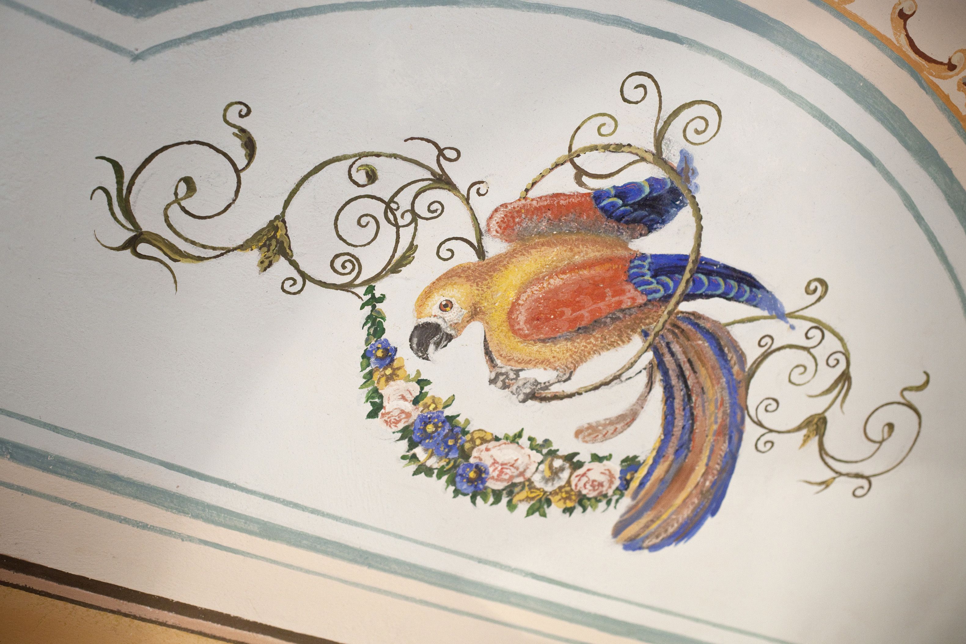 A ceiling with a painted bird surrounded by floral patterns and swirls.
