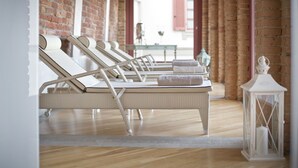 Un cuarto de spa con cuatro sillones blancos de mimbre, una mesita con un florero y un farol blanco.