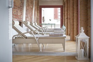 Um quarto de spa com quatro espreguiçadeiras de vime branco, uma mesa pequena com um vaso e um candeeiro branco.