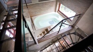 Una piscina interior con techos altos, barandilla de vidrio, paneles de madera y una escalera que conduce a niveles superiores.
