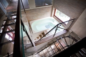 Piscina interior ampla com pé direito alto, cercada por painéis de madeira e uma escadaria que dá acesso a andares superiores, com guarda-corpo de vidro.