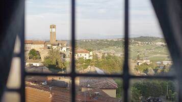 Blick durch ein Fenster auf eine Stadt mit einem markanten Glockenturm, verschiedenen Gebäuden und umgebender Grünfläche.