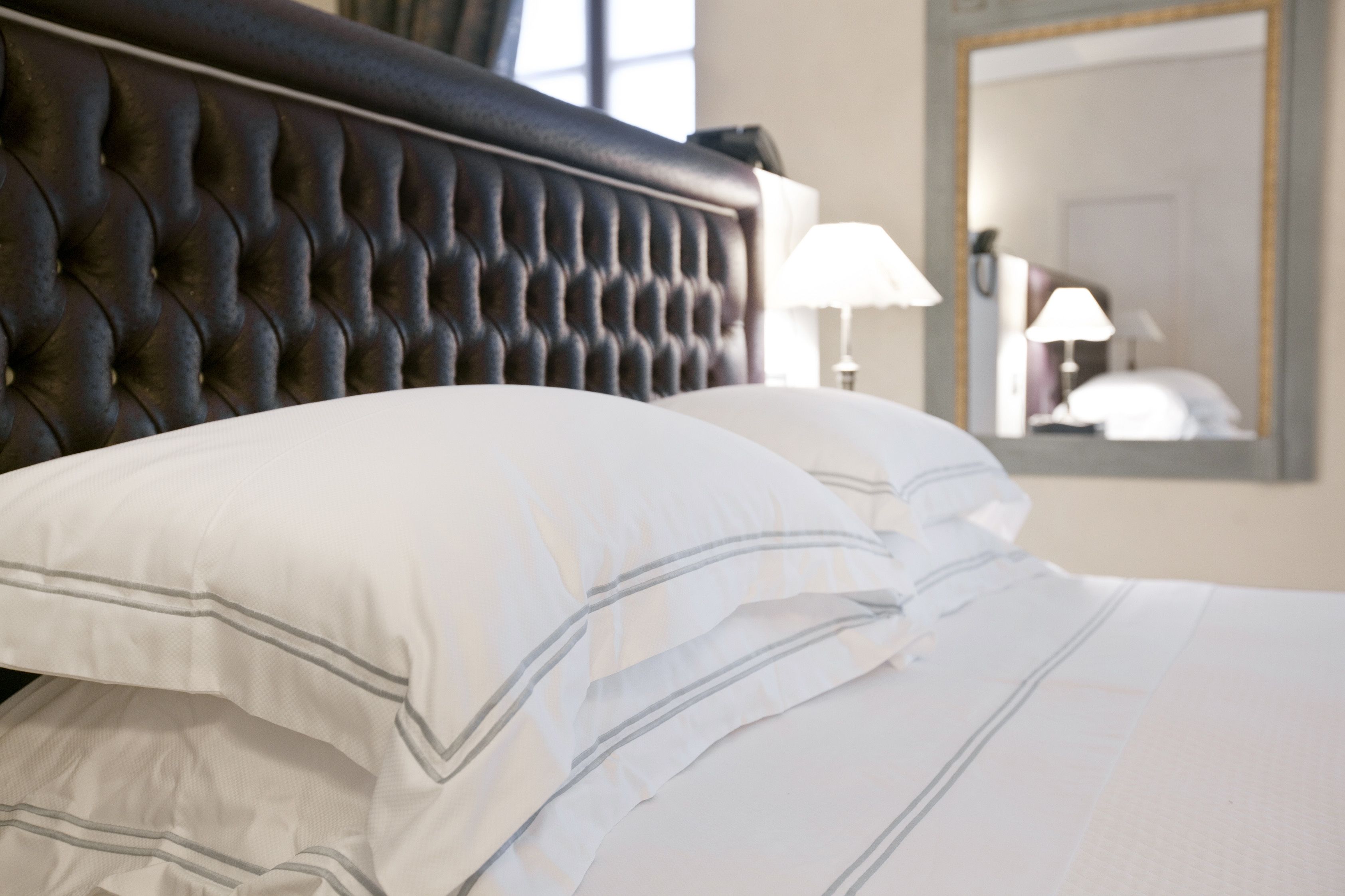 A neatly made bed with white linens and striped pillows, a tufted headboard, and a bedside lamp.