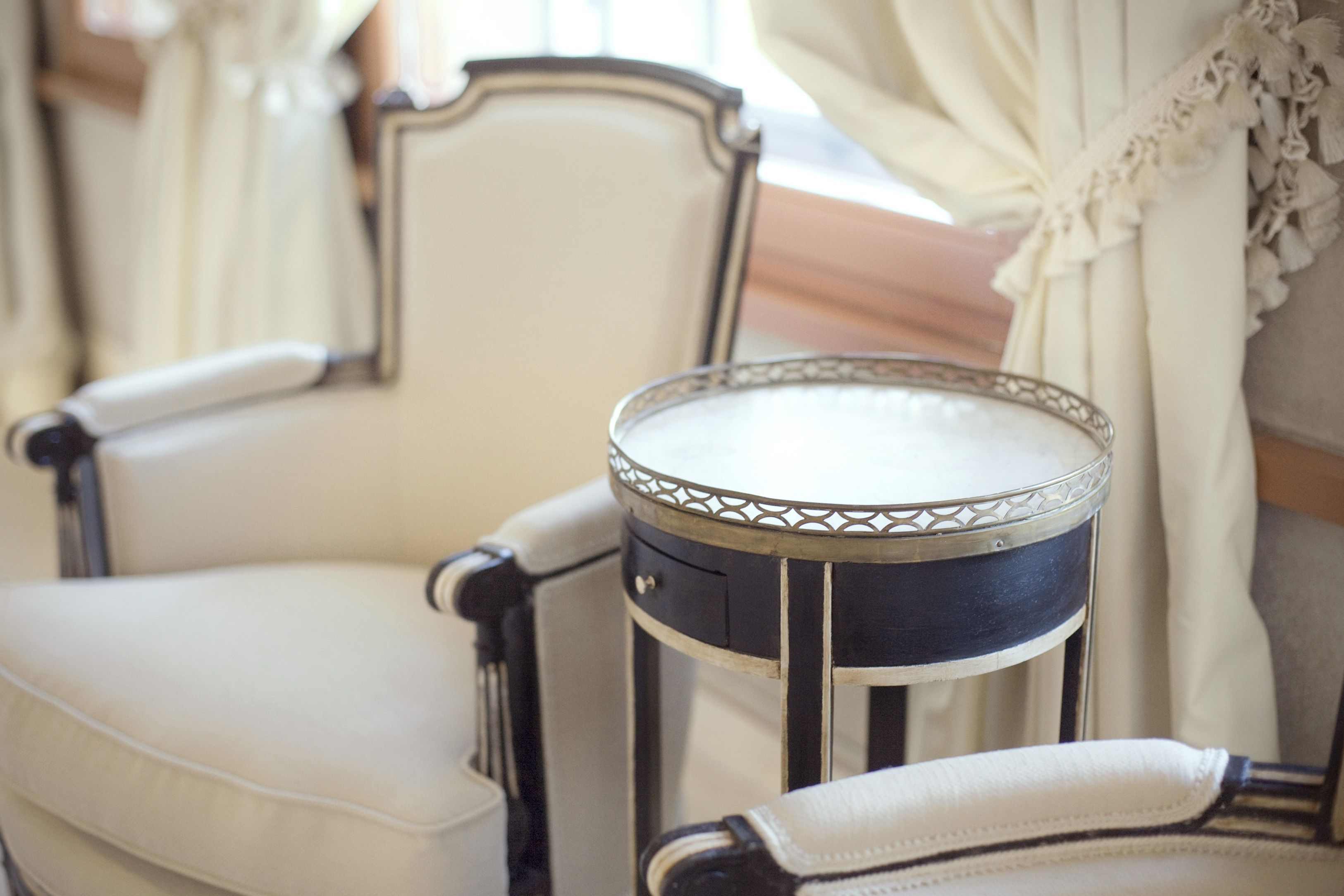 Una silla con un cojín blanco y una mesita redonda con un borde metálico decorativo.