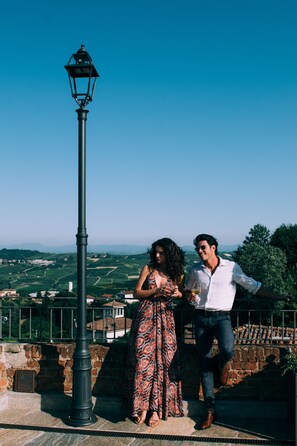 A couple standing by a street lamp overlooking a scenic landscape with buildings and greenery. - Relais Villa Prato (Mombaruzzo)