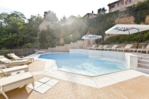 A swimming pool with lounge chairs and umbrellas, surrounded by a brick wall and greenery. - Relais Villa Prato (Mombaruzzo)