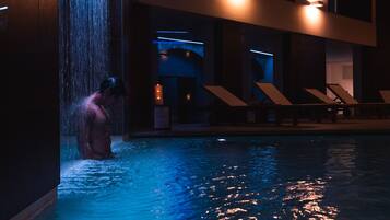 Ein Mann in einem Pool mit Wasserstrahlen, umgeben von Liegestühlen und moderner Architektur.