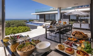 A dining area with a pool view, outdoor seating, and a variety of food and drinks. - Moondance Villa & Suites (Cape Town)