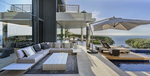 A modern outdoor living space with a pool, seating area, and a view of the ocean. - Moondance Villa & Suites (Cape Town)
