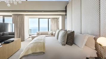 A modern hotel room with a large bed, a TV, a desk, and a view of the ocean.