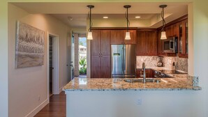 A modern kitchen with wooden cabinets, stainless steel appliances, granite countertops, and pendant lighting.