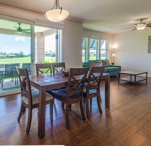 Uma sala de jantar com mesa e cadeiras de madeira, janelas amplas com persianas e vista para um campo de golfe.