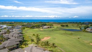 A golf course with a clubhouse, palm trees, and a view of the ocean.