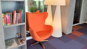 Um interior moderno com uma cadeira laranja vibrante, um abajur de chão grande e uma estante repleta de livros.
