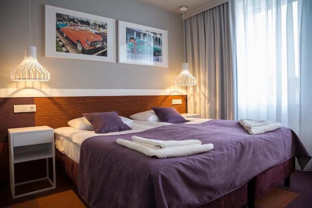 A hotel room with a double bed, two side tables, a headboard, and two wall-mounted lamps.
