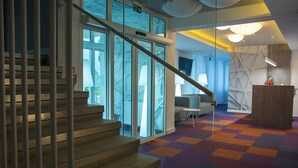 Um lobby moderno com escada, portas de vidro, um tapete colorido e móveis contemporâneos.