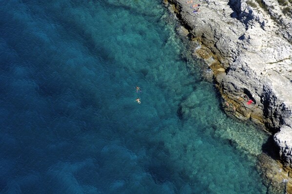 A coastal area with clear water, rocky terrain, and people swimming.