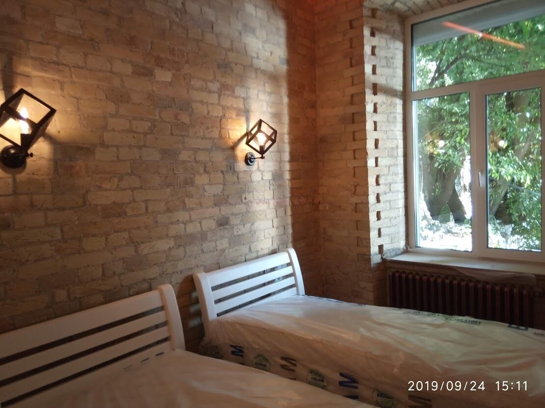 A room with a brick wall, two beds, a window with a view of trees, and two wall-mounted light fixtures.