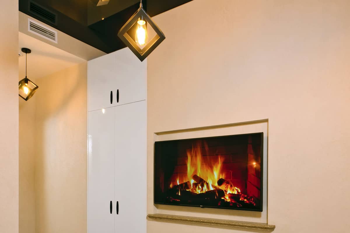 A hotel room with a bed, a framed picture of a fireplace, and pendant lights.